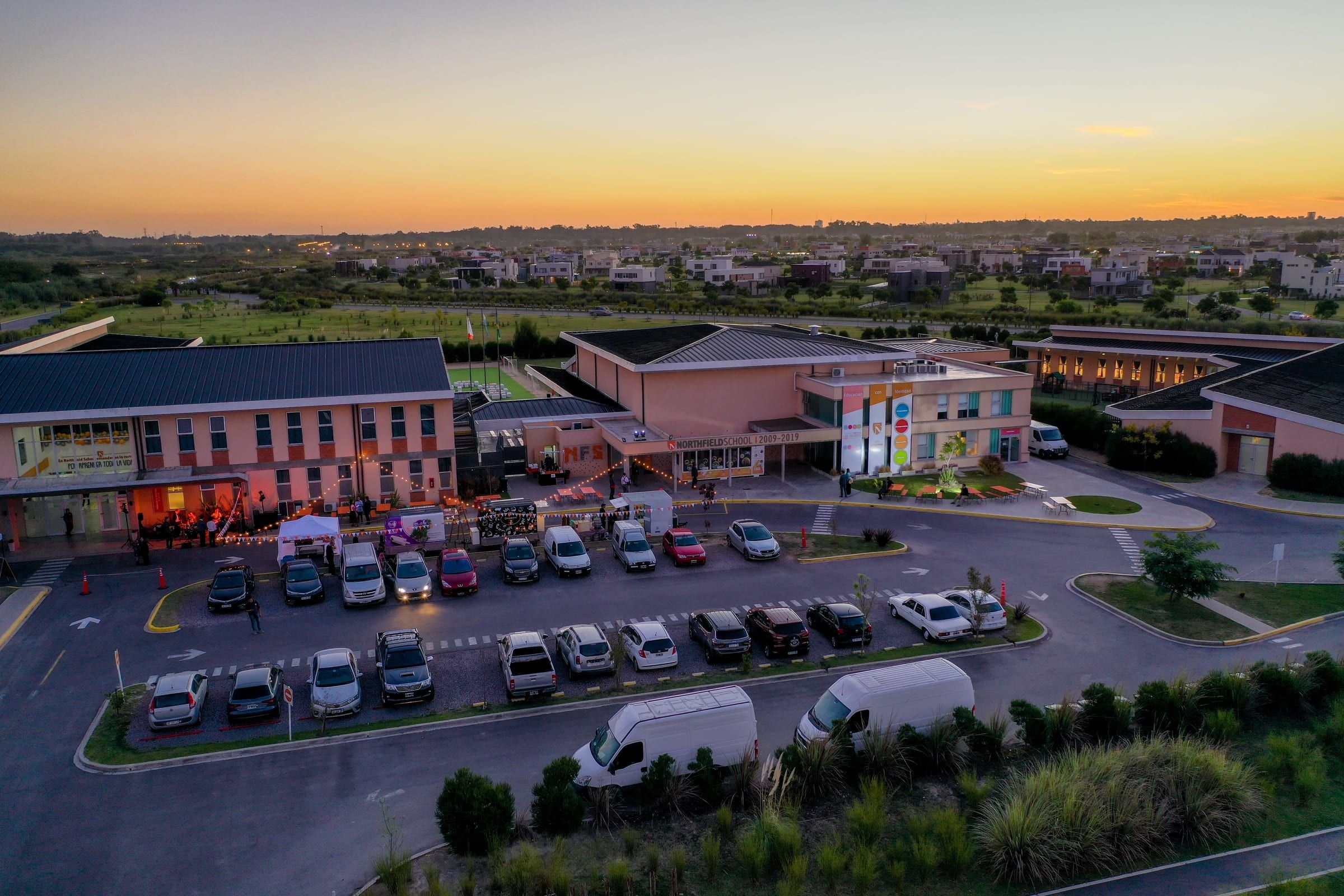 Northfield School Puertos desde el aire, al atardecer: el campus completo, con la playa de estacionamiento llena y un evento en el patio